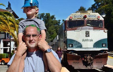 child on man's shoulders with Amtrak train behind them